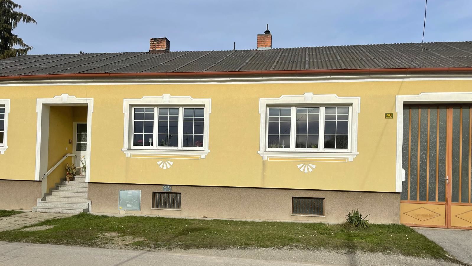 Außenansicht eines gelben Hauses mit weißen Fensterrahmen und einer Eingangstreppe.