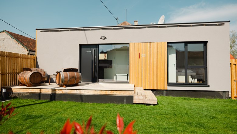 Modernes Gebäude mit Terrasse und Weinfässern im Garten.