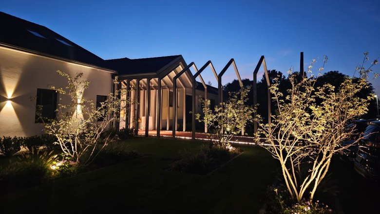 Beleuchtetes Gebäude bei Nacht mit modernen Strukturen und Bäumen im Vordergrund.