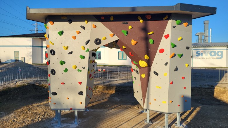 Eine freistehende Boulderwand mit bunten Klettergriffen auf einem sonnigen Gel&auml;nde.