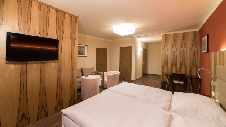 Modern eingerichtetes Hotelzimmer mit Doppelbett, Fernseher, Sitzbereich und Holzmöbeln.