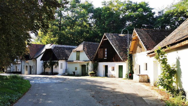 Eine malerische Gasse mit traditionellen weißen Häusern und schrägen Dächern, umgeben von Bäumen.