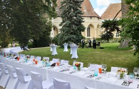 Gedeckte Tische im Freien vor einem historischen Gebäude mit Musikern im Hintergrund.