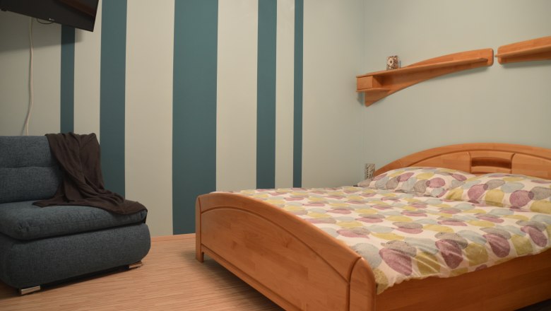 Schlafzimmer mit gestreifter Wand, Holzbett und Sofa.