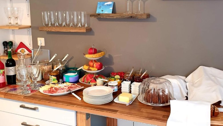 Frühstücksbuffet mit Gläsern, Obst, Aufschnitt und Kuchen.