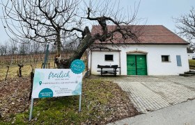 Weißes Gebäude mit grünem Tor und Schild 'freilich' in einer ländlichen Umgebung.