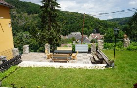 Terrasse mit Holzmöbeln und Blick auf ein Dorf und bewaldete Hügel.