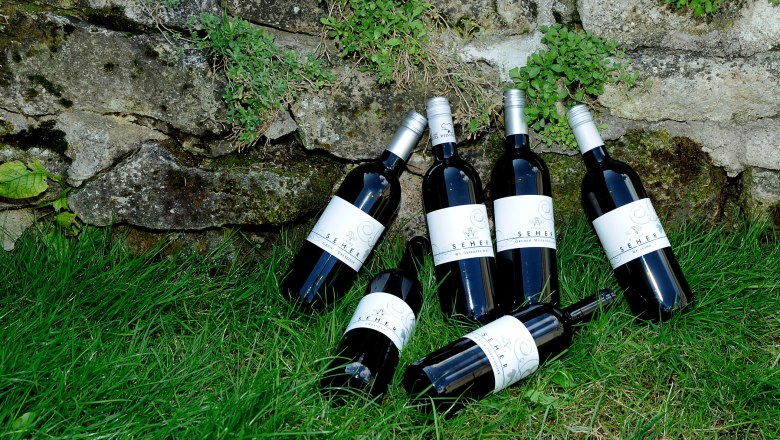 Wine, © Seher Six wine bottles on grass in front of a stone wall.