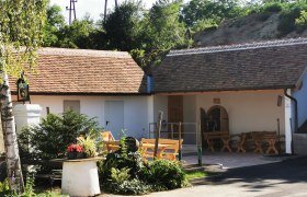 Ein gemütlicher Außenbereich mit Holzbänken und Pflanzen vor einem Gebäude mit Ziegeldach.