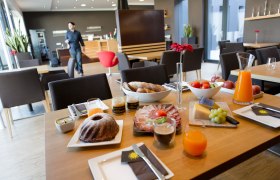 Frühstückstisch mit Gebäck, Aufschnitt, Käse, Obst und Saft in einem modernen Café.