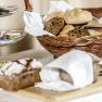 A breakfast table with a basket full of bread rolls, a bread cutting board and a tray of jams.