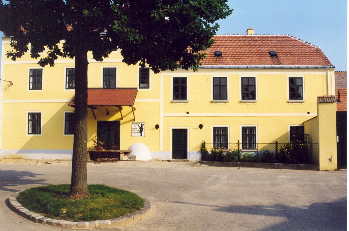 Gelbes Gebäude mit rotem Dach und Baum im Vordergrund.