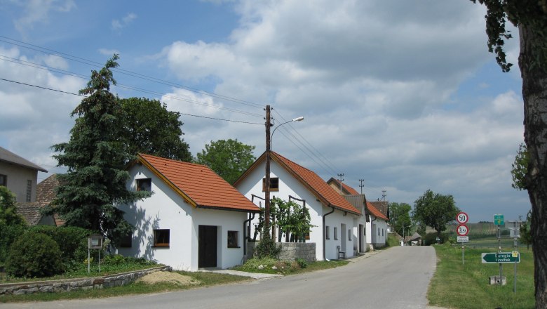 Kellergasse in Großkadolz mit weißen Häusern und rotem Dach entlang einer Straße.