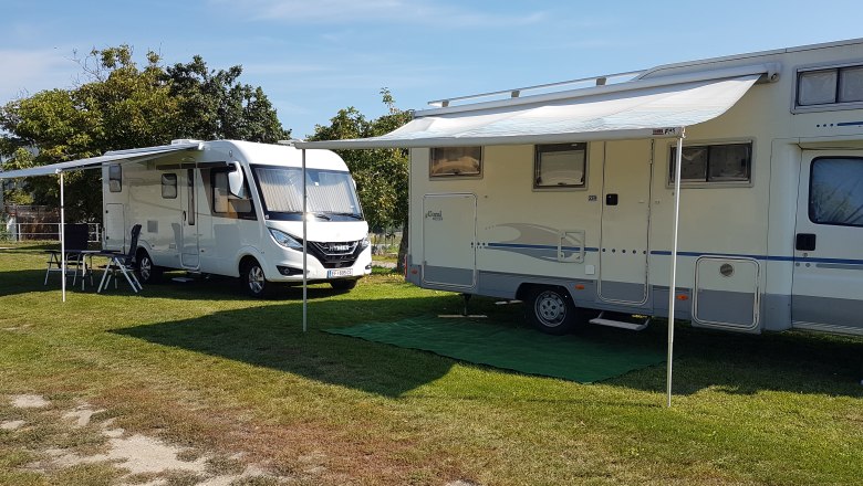 Zwei Wohnmobile mit ausgefahrenen Markisen auf einem Campingplatz.