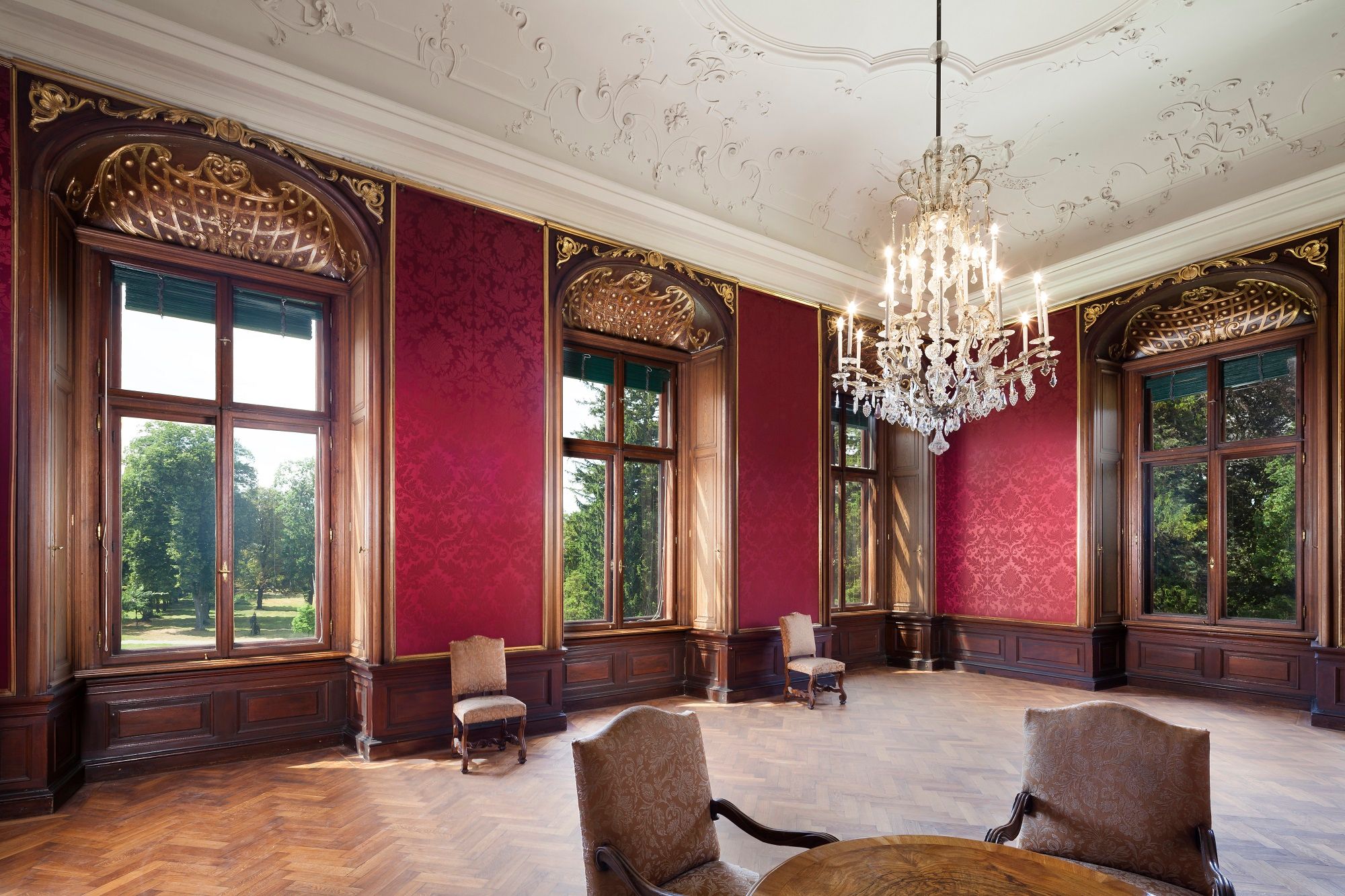 Elegant room in Eckartsau Castle with red walls, large windows and a chandelier.
