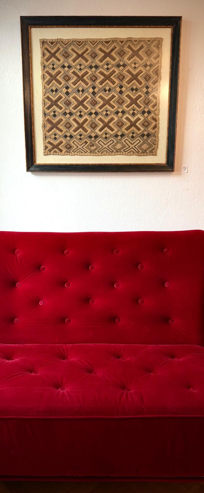 Rotes Sofa vor einem gerahmten, gemusterten Kunstwerk an der Wand.