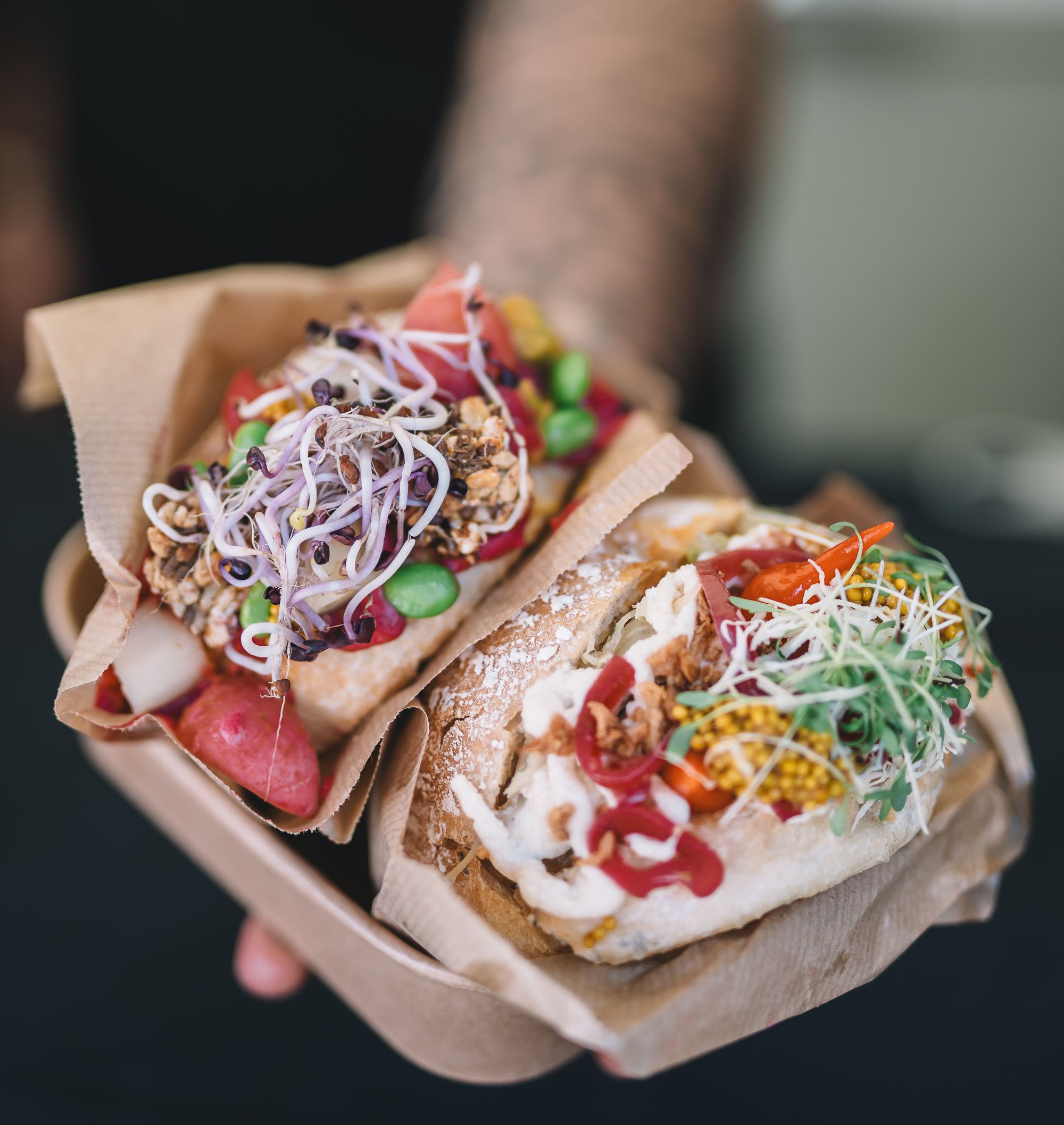 Eine Person hält zwei Winzerweckerl, gefüllt mit regionalen Produkten wie frischem Gemüse, Sauerkraut und mehr, in die Kamera. 