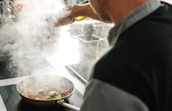 In der dampfenden Küche entfaltet sich der verführerische Duft frischer Zutaten, während ein Koch mit Hingabe Gemüse in einer Pfanne anbrät. Die Atmosphäre ist lebhaft und einladend, perfekt für Genießer, die die kulinarischen Köstlichkeiten der Region entdecken möchten.