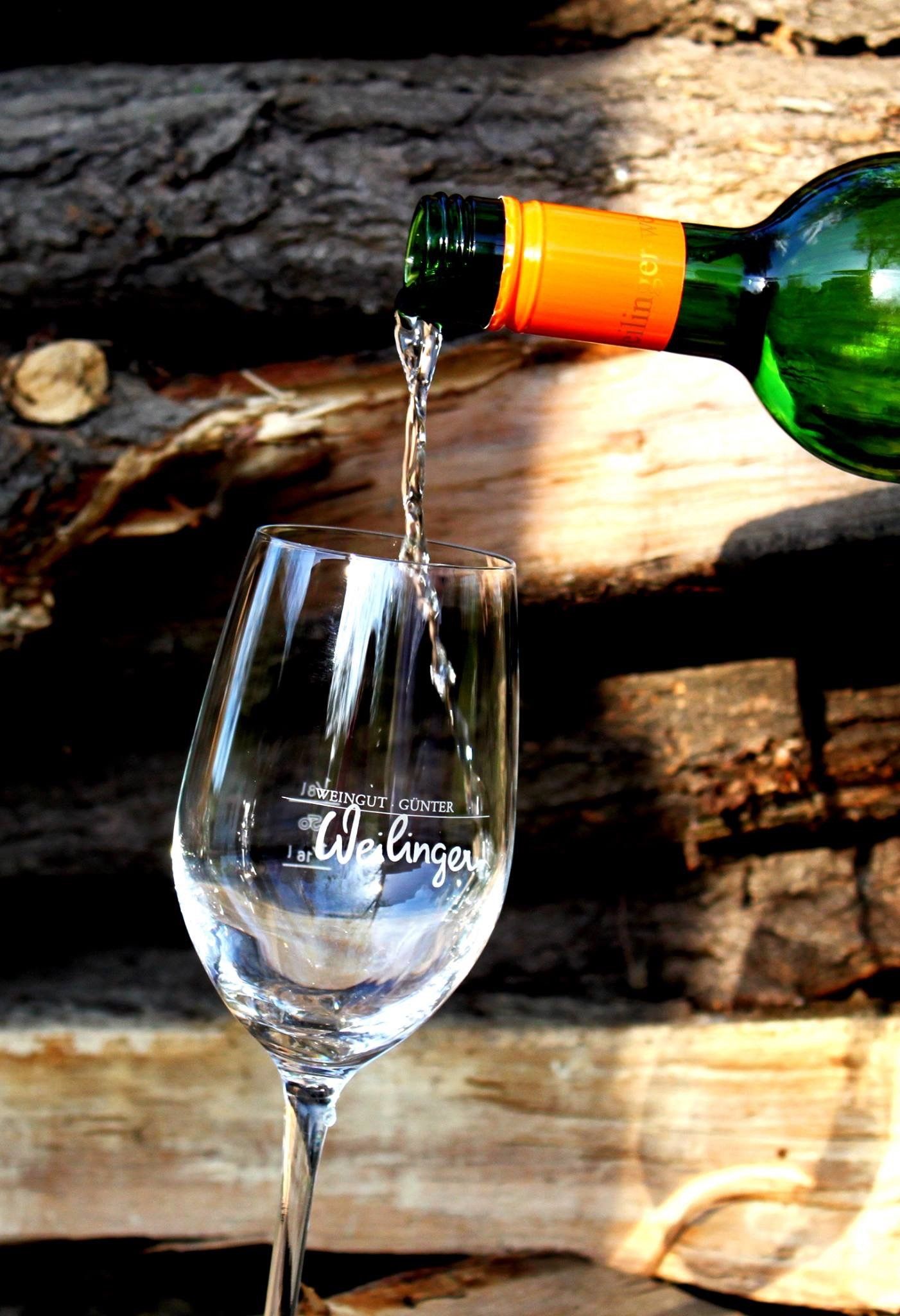 A glass of wine is poured from a bottle with an orange cap. Logs can be seen in the background.