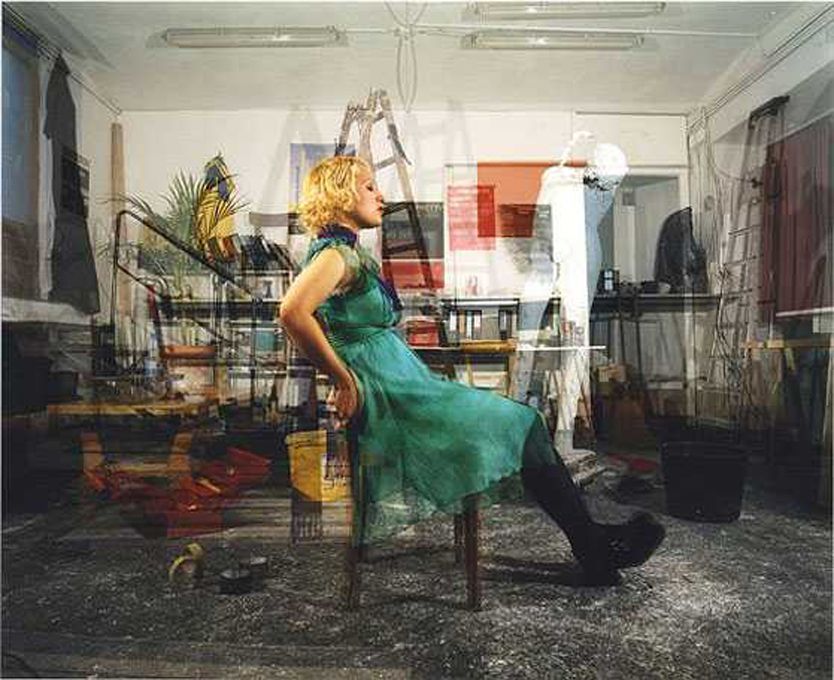 Eine Frau in einem grünen Kleid sitzt in einem überfüllten Raum auf einem Stuhl.