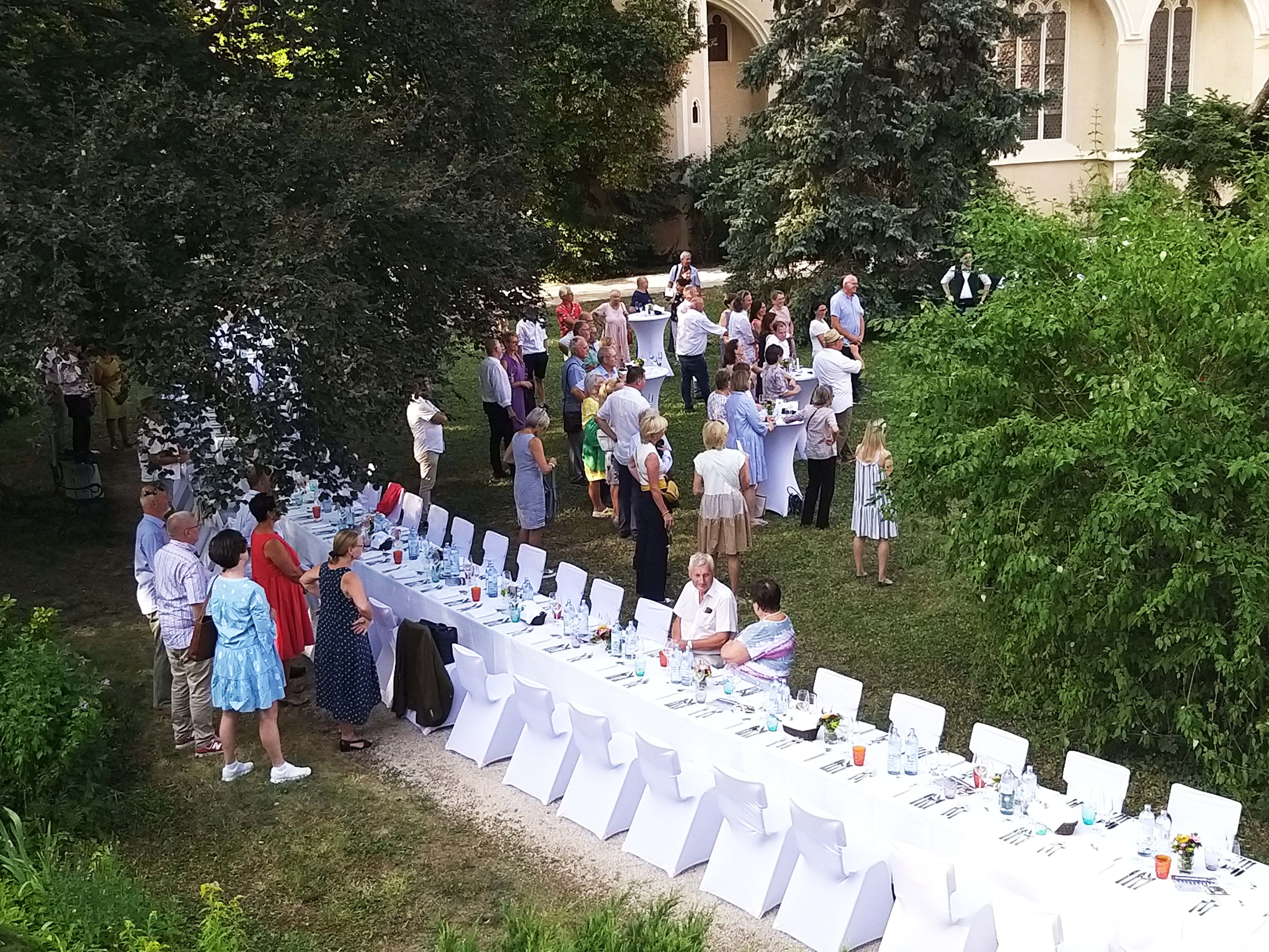 Menschen bei einer Gartenfeier mit langen, gedeckten Tischen im Freien.