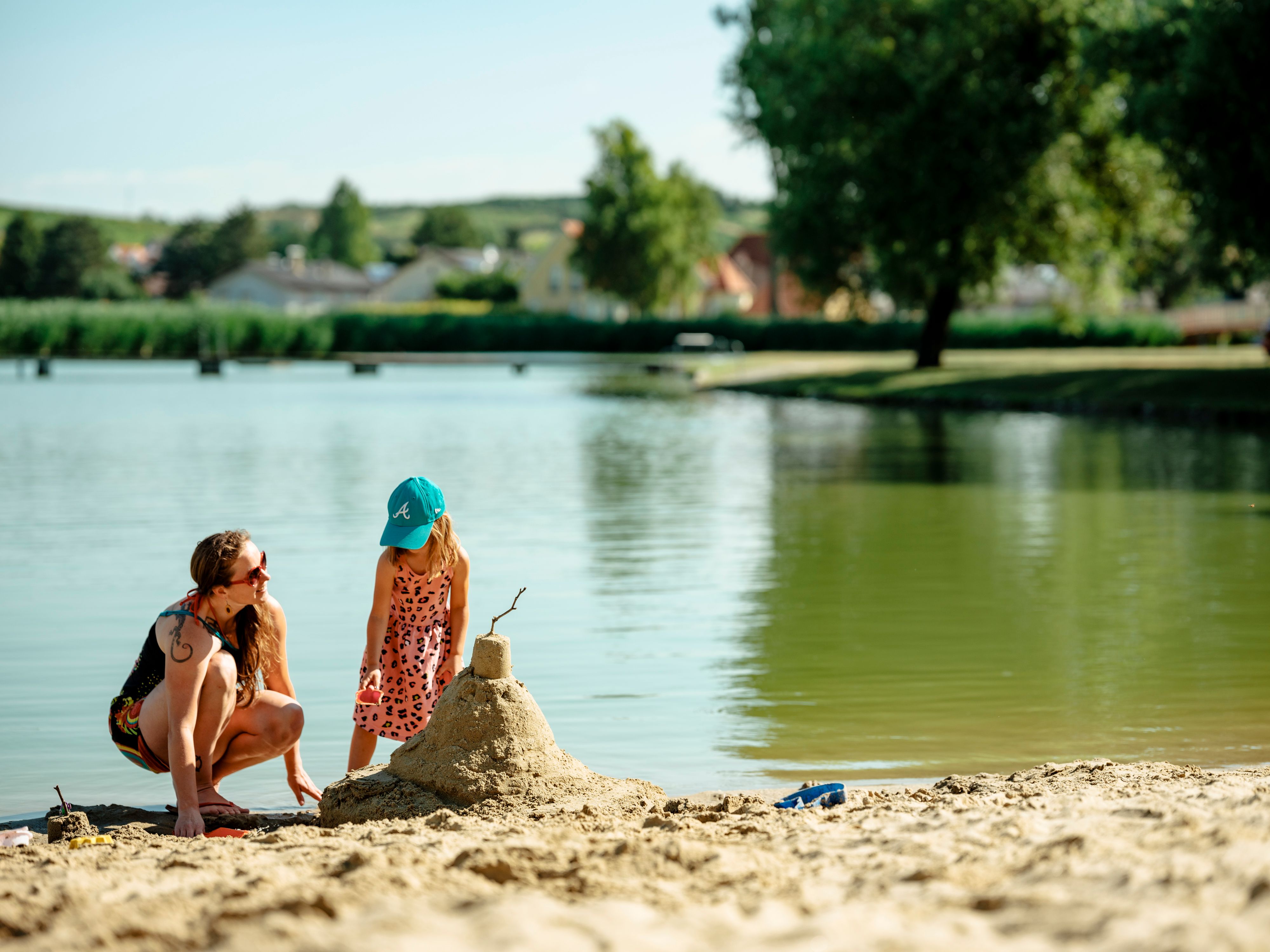 Eine Frau und ein Kind bauen eine Sandburg am Ufer eines Badeteichs.