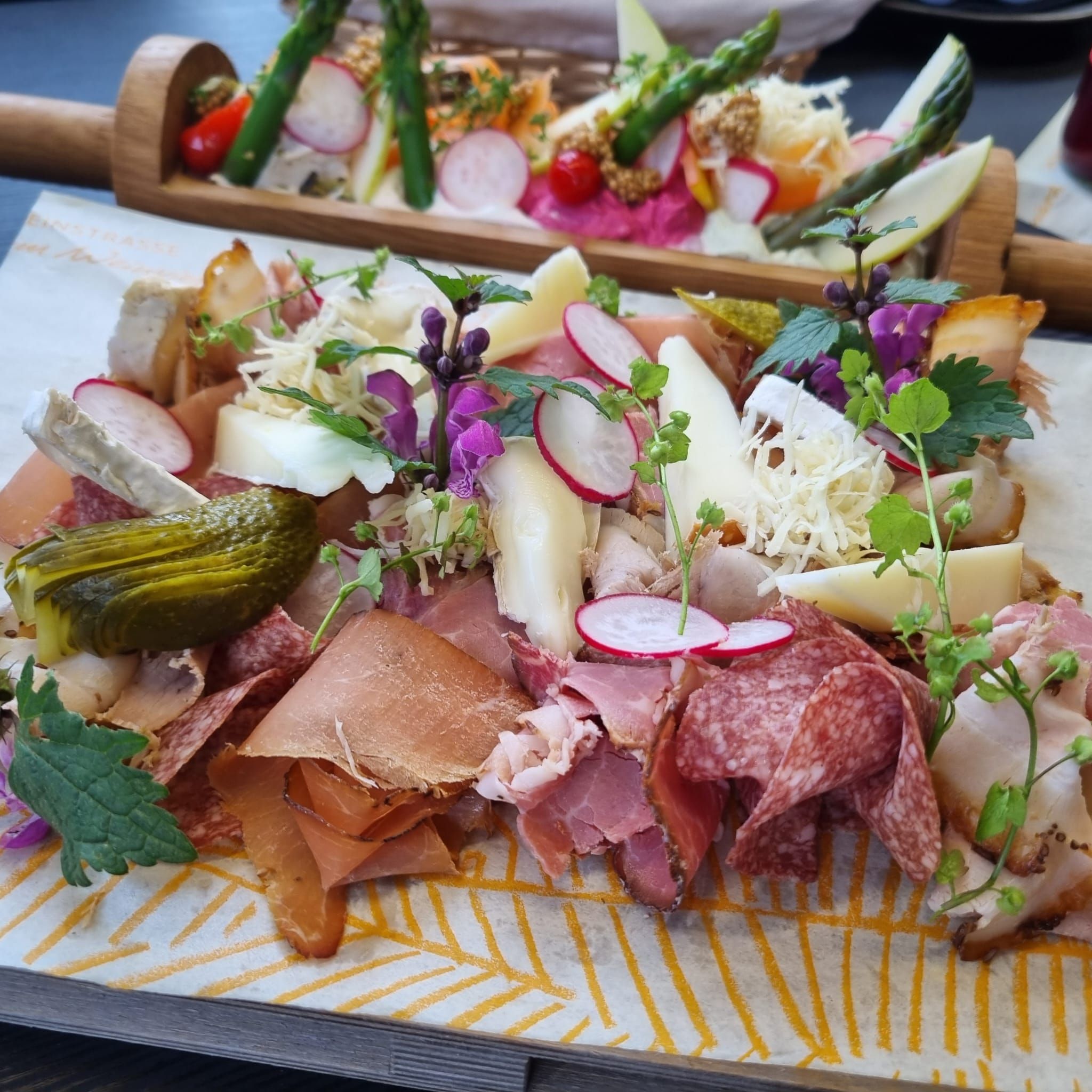 Eine Heurigenplatte mit verschiedenen Wurst- und Käsesorten, Radieschen, Essiggurken und Kräutern auf einem Holzbrett serviert.