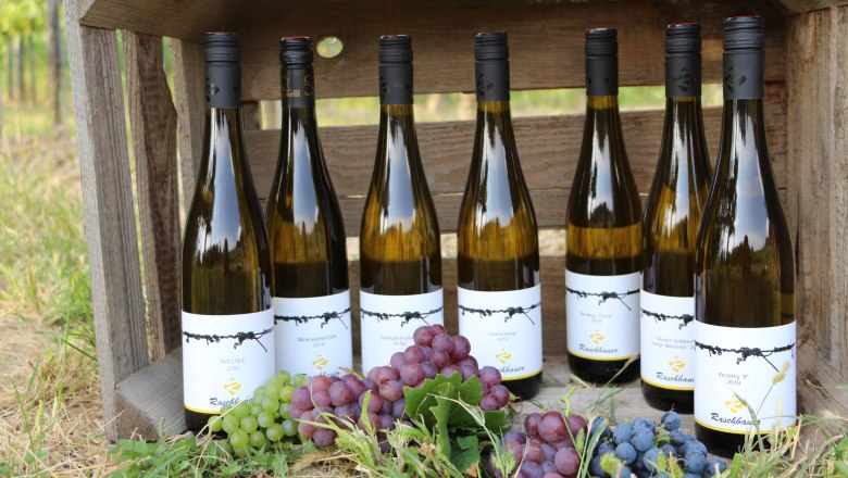 Sieben Weinflaschen in einer Holzkiste mit Trauben im Vordergrund.