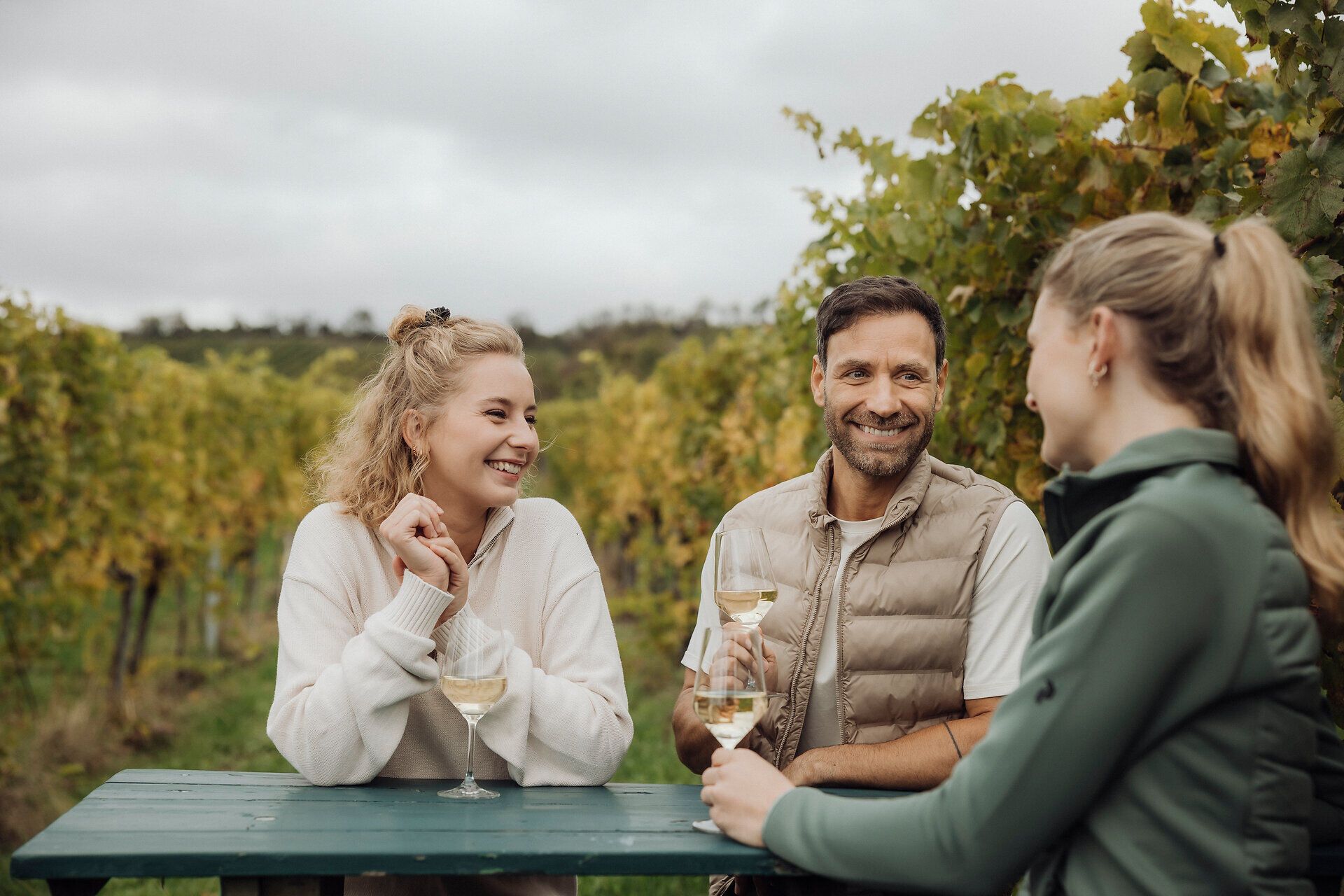 Inmitten der sanften Hügel des Weinviertels genießen drei Freunde ein entspanntes Zusammensein bei einem Glas Wein. Umgeben von üppigen Weinreben und der frischen Luft der Natur, strahlt die Szenerie eine herzliche und gesellige Atmosphäre aus, die zum Verweilen einlädt.