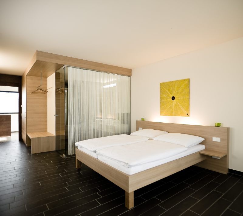 Modernes Hotelzimmer mit Doppelbett, Holzmöbeln und Glaswand.