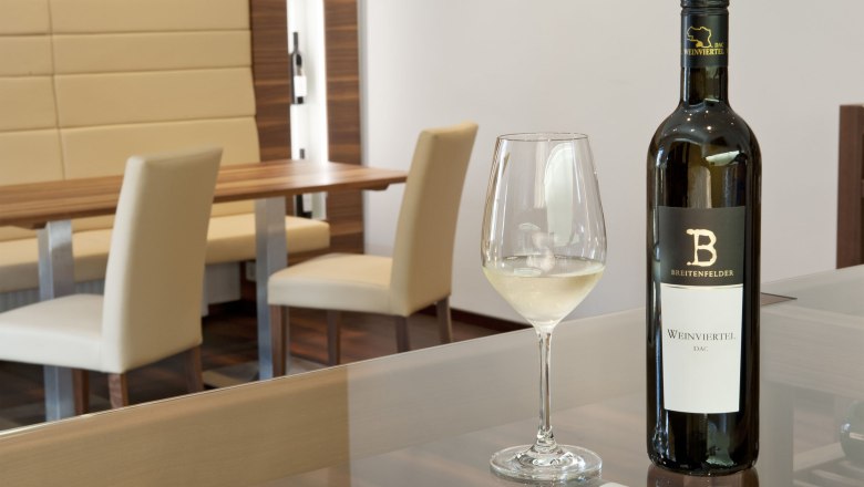 Ein Verkostungsraum mit einer Flasche Weißwein und einem gefüllten Weinglas auf einem Tisch.