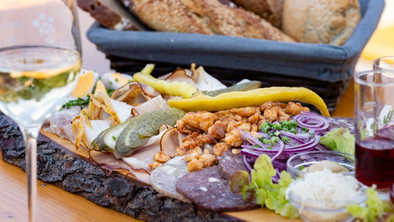 A Heurigen platter with various types of sausage, onions, gherkins and bread on a wooden table.