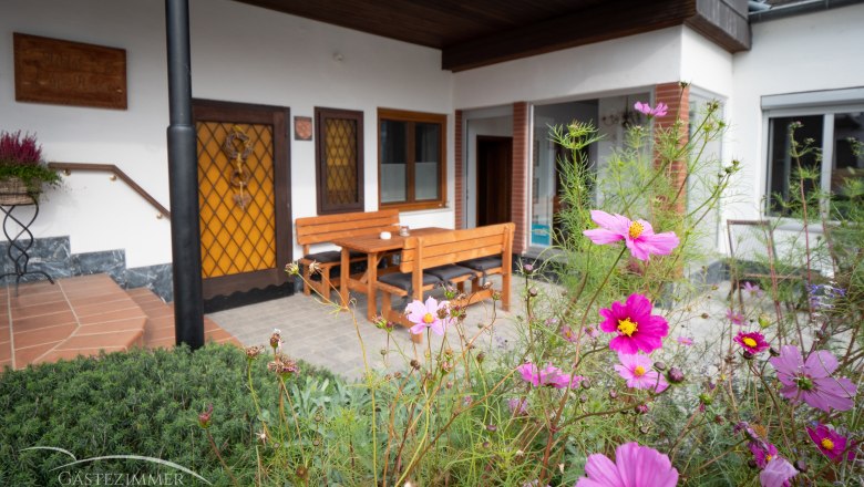 Terrasse mit Holzmöbeln und blühenden Blumen im Vordergrund.