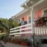 Eine Person steht auf einer Veranda eines rosa Hauses mit Blumen und hält ein Schild.