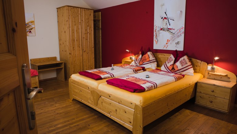 Gemütliches Gästezimmer mit Doppelbett, Holzmöbeln und roter Wand.