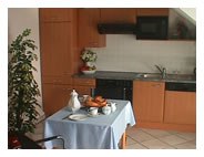 Kleine Küche mit Holzmöbeln, Esstisch mit blauer Tischdecke und Geschirr.