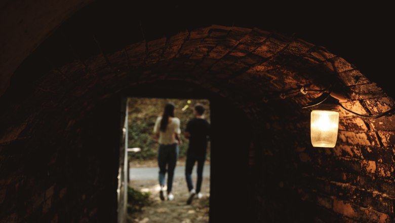 Blick aus einem dunklen Tunnel auf zwei Personen im Freien.