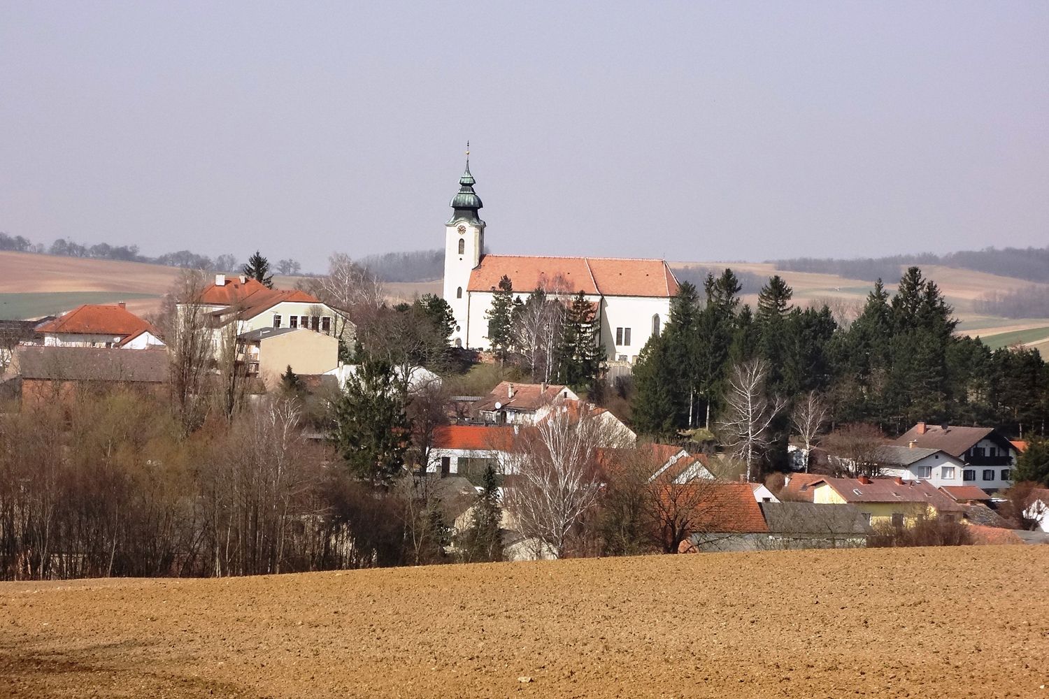 Blick auf das Dorf Gnadendorf mit Kirche und umliegenden Häusern in ländlicher Landschaft.