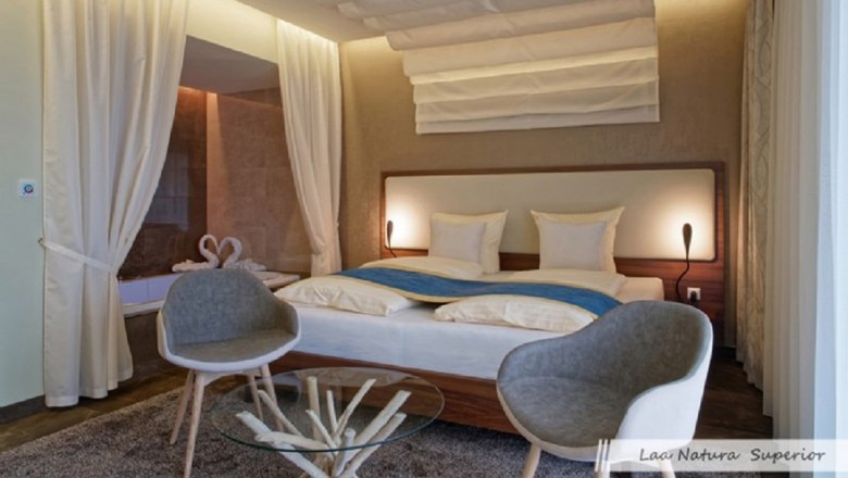 Modernes Doppelzimmer mit großem Bett, zwei grauen Stühlen und einem Glastisch.