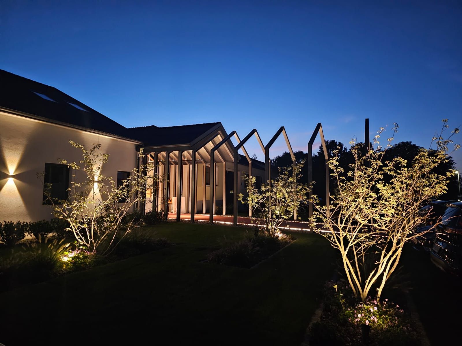 Beleuchtetes Gebäude bei Nacht mit modernen Strukturen und Bäumen im Vordergrund.