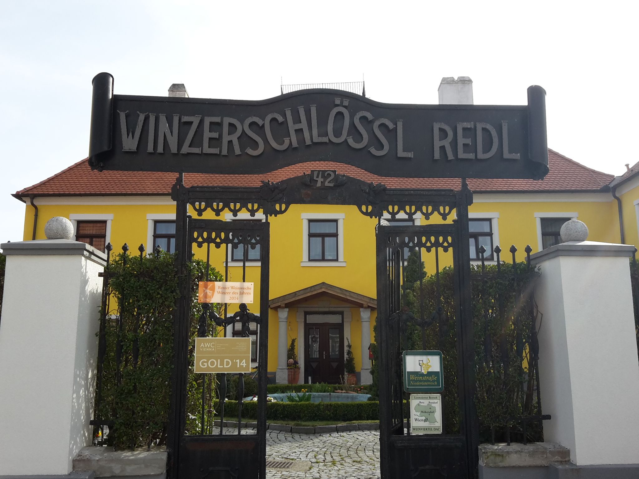 Entrance gate to Winzerschlössl Redl with yellow building in the background.