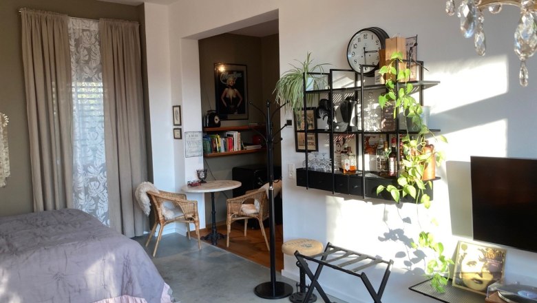 Gemütliches Wohnzimmer mit Bett, Regal, Pflanzen und Wanddekoration.