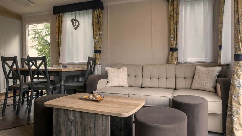 Gemütliches Wohnzimmer mit beiger Couch, Holztisch und Essbereich im Hintergrund.