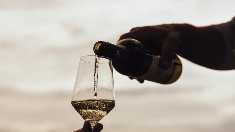 Wein wird in ein Glas im Freien eingeschenkt, im Hintergrund eine Landschaft.