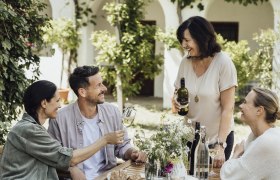 Vier Personen sitzen an einem Tisch im Freien und genießen Wein und Brot.