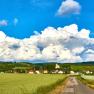 Landschaft mit Dorf, Feldern und Kirche vor großen Wolken.