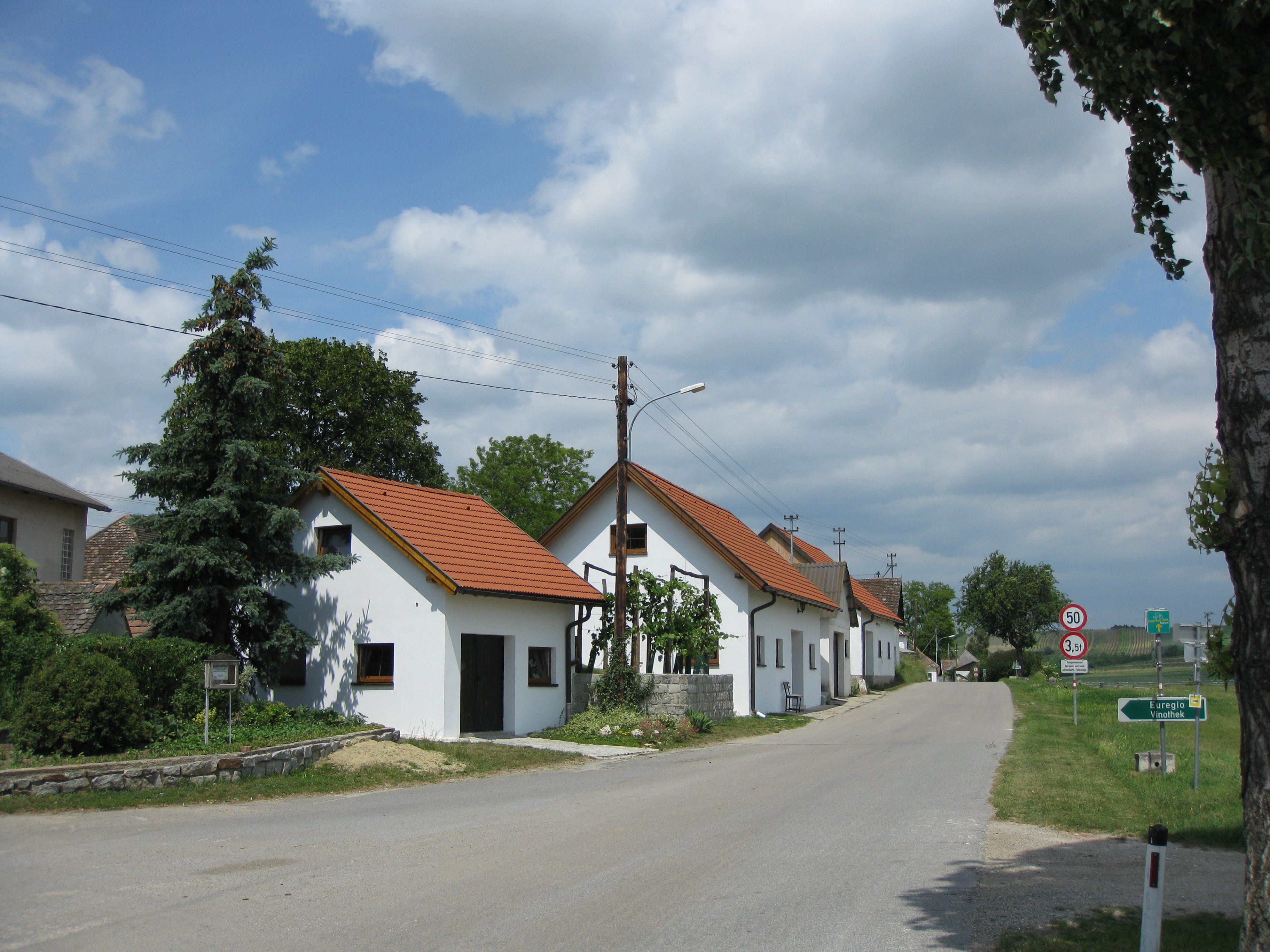 Kellergasse in Großkadolz mit weißen Häusern und rotem Dach entlang einer Straße.