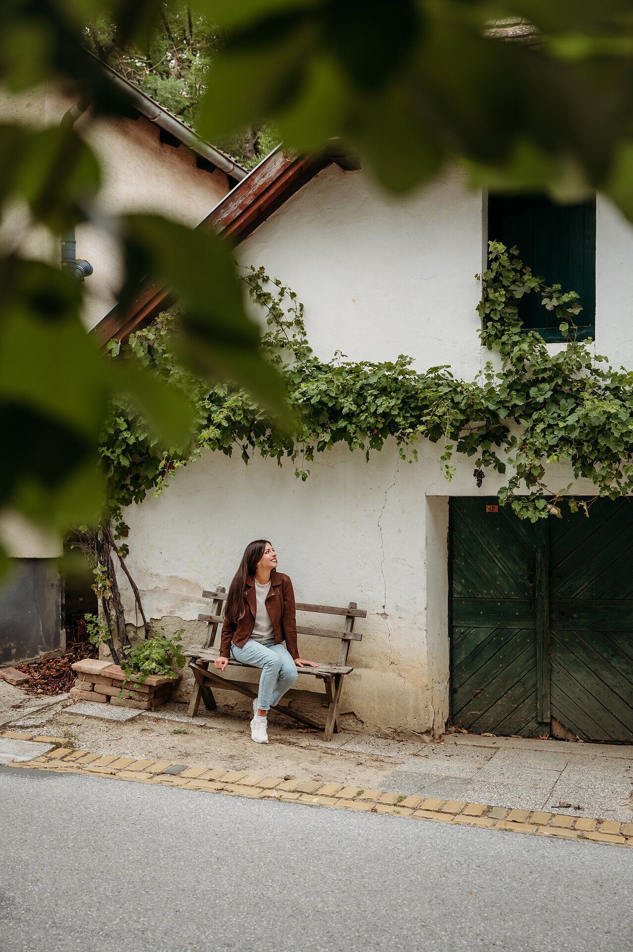 Eine Frau sitzt auf einer Holzbank vor einem Presshaus und blickt sich in der Kellergasse um.