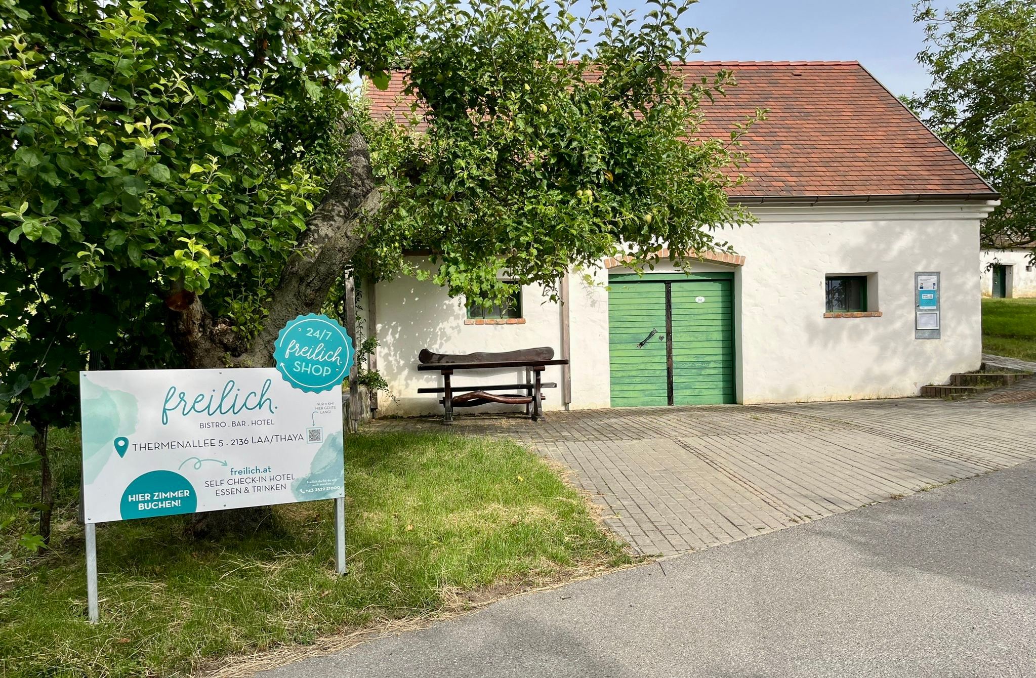 Außenansicht des freilich.-Gebäudes mit grünem Tor, Schild und Bäumen davor.
