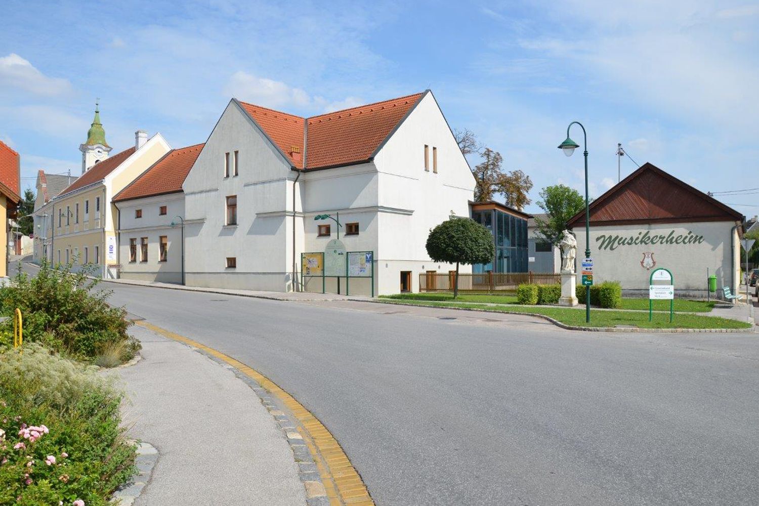 Straßenszene in Hohenruppersdorf mit Musikerheim und Kirche im Hintergrund.